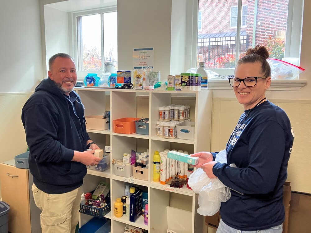 Two DRBA employees stand in front of shelves filled with "Most Needed Items"