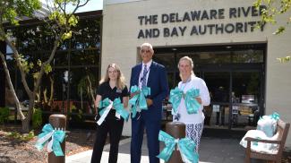 Joel Coppage, Executive Director of the DRBA, holds up teal bows with staff in front of the Delaware River and Bay Authority's headquarters