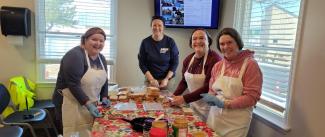 DRBA employees and employees from Shephard's Office pose together in hair nets around a table while they make PB & Js	