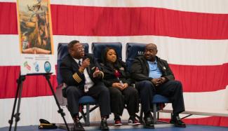 3 speakers at the Tuskeegee event presenting on stage with an American flag in the background